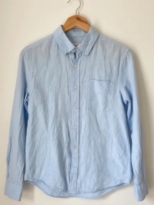 Ljusblå linneskjorta från Dressmann storlek S - Säljer en ljusblå skjorta från Dressmann i linnemix. Skjortan har klassisk krage, bröstficka och knappar framtill. Perfekt för dig som gillar en enkel och stilren look. Storlek S.