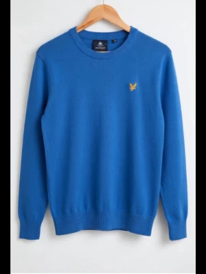 Blå stickad tröja från Lyle & Scott storlek S - Säljer en blå stickad tröja från Lyle & Scott med deras klassiska gula logotyp på bröstet. Tröjan har rund hals och långa ärmar, perfekt för dig som gillar stilrena och enkla plagg. Ribbstickad nederkant och ärmslut ger en snygg passform.