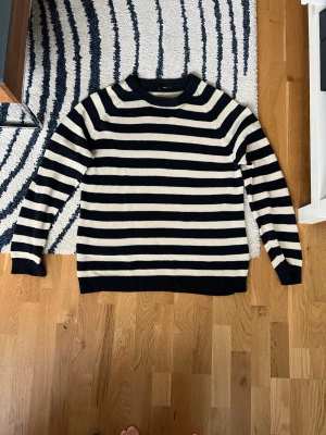 Randig stickad tröja från Filippa K - Snygg stickad tröja från Filippa K med breda marinblå och vita ränder. Tröjan har rund halsringning och långa ärmar. Perfekt för dig som gillar klassisk och stilren design. Materialet känns mjukt och bekvämt. Linne 55% och bomull 45%