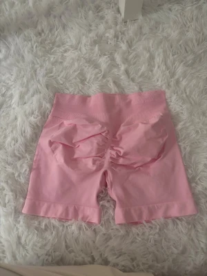 Rosa seamless shorts med scrunch - Säljer ett par ljusrosa seamless shorts med scrunch-detalj bak och hög midja. De är stretchiga och bekväma, perfekta för träning eller chill. Materialet känns mjukt och följsamt mot huden.