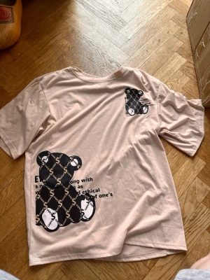 Beige t-shirt med björnmotiv - Snygg beige t-shirt med svart och vitt björnmotiv framtill och textdetaljer. T-shirten har korta ärmar och en relaxed passform. Tillverkad i mjuk bomull, perfekt för en chill och trendig look. Skriv gärna för mått! 💕