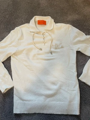 Vit tröja från La Martina Gerard Loft - Snygg vit tröja från La Martina Gerard Loft med krage och snörning vid halsen. Tröjan har ett broderat LM på bröstet och ribbade muddar vid ärmslut och nederkant. Perfekt för dig som gillar stilrena plagg.                                                                          Endast använda 2-3 gånger.                                          Orginalpris ca. 2400kr