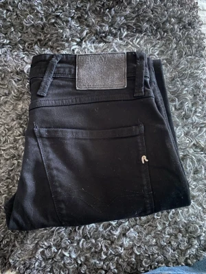 Svarta jeans från Replay - Snygga svarta jeans från Replay med klassisk femficksmodell och raka ben. Jeansen har bälteshällor, diskret Replay-logga på bakfickan och svart patch bak i midjan. Materialet är mjukt och stretchigt för skön passform.