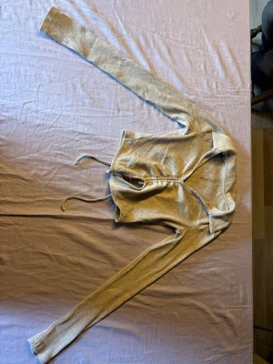 Beige ribbad omlottkofta - Trendig beige ribbad omlottkofta med långa ärmar och knytband i midjan. Koftan har en smickrande croppad passform och mjukt, stretchigt material som sitter snyggt på kroppen. Perfekt att styla över ett linne eller topp.