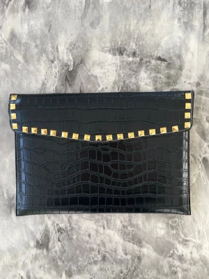 Datorfodral i krokodil mönster med guldnitar  - Stilrent datorfodral tillverkat av veganskt läder i vattentätt material. Fodralet stängs med knapp. Fodralet skyddar din dator effektivt samtidigt som det ger din outfit en extra touch. ⚜️ Storlek: 34 × 25 cm –  Innifrån 33 x 24 📦  