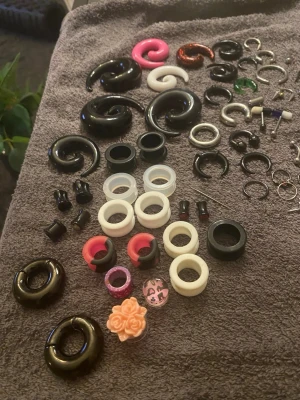 Stort mixpaket med piercingar och töjningar - Säljer ett stort mixpaket med olika piercingar , töjningar och tunnels i flera färger och former. Innehåller spiraler, ringar, pluggar och tunnels i svart, vitt, rosa, orange, lila och transparent. Materialen varierar mellan plast, akryl och metall. Perfekt för dig som gillar att byta stil ofta! Från 0,8mm till 18mm. Du kan välja mellan och köpa vissa piercingar eller hela paketet med alla piercingar. 