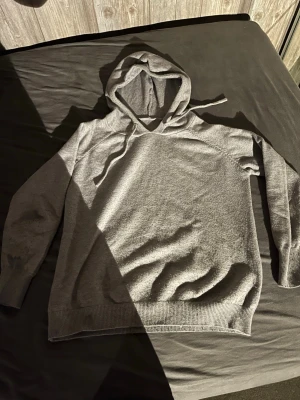 Grå hoodie med dragsko - En enkel och stilren grå hoodie med huva och dragsko. Hoodien har långa ärmar, ribbade muddar vid ärmslut och nederkant. Perfekt för en avslappnad look och passar till det mesta. Materialet känns mjukt och bekvämt mot huden.