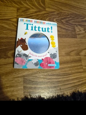 Tittut! Min första spegelbok - En färgglad pekbok för små barn med titeln 'Tittut!'. Boken har ett spegelinslag på framsidan och söta illustrationer av djur som ko, häst och får. Perfekt för lekfull läsning och upptäckt. Boken är i kartong och har tydliga färger och former.