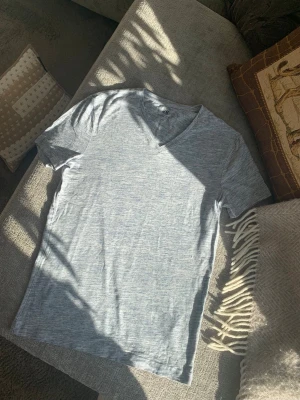 Ljusgrå v-ringad t-shirt från H&M - Säljer en stilren ljusgrå, ljusblå melerad t-shirt med v-ringning och korta ärmar. T-shirten har en enkel och clean look, perfekt till jeans eller shorts. Materialet är supermjukt.