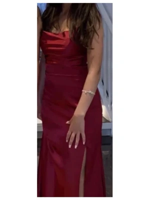 Vinröd balklänning med öppen rygg och slits  - Elegant vinröd långklänning med slits framtill och öppen rygg med snygg snörning det är även en inbyggd bh i klänningen så att man slipper ha en bh som täcker ryggen. Klänningen har smala axelband som korsas i ryggen och en figurnära passform. Tillverkad i ett glansigt material. Pris går att diskutera 🙏