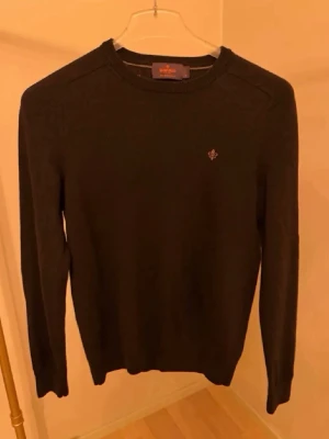 Mörkbrun stickad tröja Morris - Snygg mörkbrun stickad tröja från Morris med rund halsringning och diskret logga broderad på bröstet. Tröjan har långa ärmar och ribbade muddar vid ärmslut och nederkant. Perfekt för lager på lager och enkel att matcha.