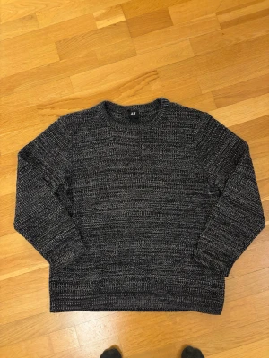 Mörkgrå stickad tröja från H&M - Säljer en mörkgråmelerad stickad tröja från H&M. Tröjan har rund halsringning, långa ärmar och ett grovt stickat mönster i svart och vitt. Perfekt för kyliga dagar och enkel att matcha med jeans eller kjol.