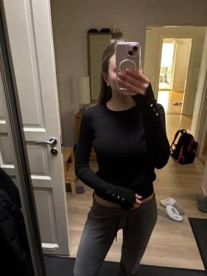 Svart långärmad topp med knappar - Svart långärmad topp med rund hals och dekorativa knappar längs ärmsluten. Snygg och enkel modell som sitter tight och passar perfekt till både jeans och kjol.