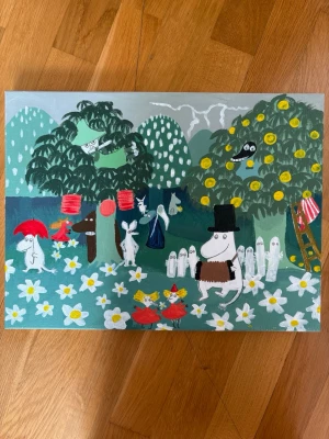 Muminmålning med klassiska figurer - Handmålad tavla med Muminmotiv på rektangulär canvas. Motivet visar flera klassiska Muminfigurer bland gröna kullar, vita blommor och träd med gula detaljer. Färgerna är främst grönt, vitt, gult. Jag har målat den själv!