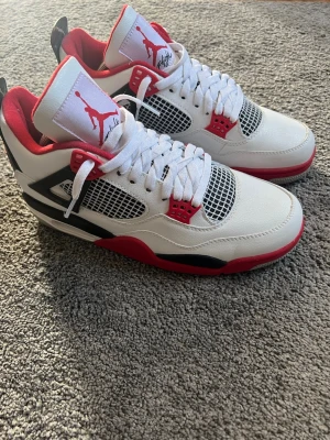 Air Jordan 4 Retro Fire Red sneakers - Säljer ett par Air Jordan 4 Retro Fire Red sneakers i vitt, rött och svart läder. Klassisk siluett med meshpaneler, röda detaljer och Jumpman-logga på plösen. 