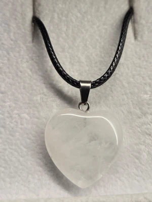 Halsband med hjärta i vit sten - Snyggt halsband med ett hjärtformat hänge i vit, halvt genomskinlig sten eller harts. Hänget sitter på ett svart, flätat band med metallfäste. Perfekt accessoar för dig som gillar stilrena och unika smycken. Passar till många olika outfits och ger en cool touch.