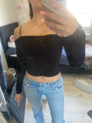 Svart offshoulder croppad topp - Trendig svart offshoulder topp med lång ärm och croppad passform. Perfekt till jeans eller kjol för en snygg och enkel look. Tunn och mjuk i materialet, sitter tight och framhäver axlarna.