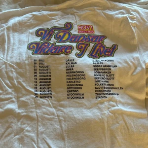 Vit Hov1 turné t-shirt Vi Dansar Vidare - Hej! Säljer min vita t-shirt från Hov1 med färgglatt tryck 'Vi Dansar Vidare I Livet' och turnédatum på ryggen från deras sista turné sommaren 2025.  Den är i storlek S, men stor i storleken så passar även M! Aldrig använd 
