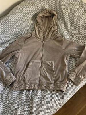 Beige hoodie med dragkedja - Säljer en beige hoodie med dragkedja framtill och fickor på magen. Hoodien har långa ärmar med resår vid ärmslut och nederkant. Perfekt för en avslappnad och stilren look. Materialet känns mjukt och bekvämt.