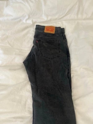 Svarta Levi's 501 jeans - Säljer ett par klassiska svarta Levi's 501 jeans med raka ben och hög midja. Jeansen har fem fickor, knappgylf och den ikoniska läderlappen bak i midjan. Tillverkade i kraftig denim med en snygg tvättad finish. Perfekta för en avslappnad och stilren look.