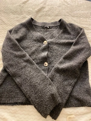 Mörkgrå kofta från Lager 157, XS - Mysig mörkgrå kofta från  lager 157 med två stora knappar framtill. Koftan har en enkel, rak passform och är tillverkad i ett mjukt, stickat material. Perfekt att slänga över en t-shirt för en avslappnad look.