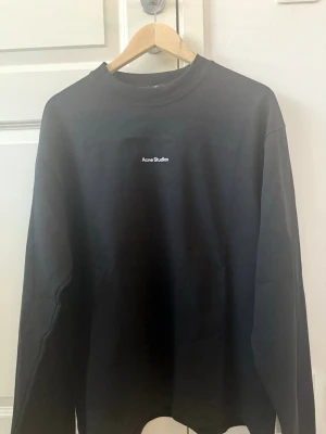 Svart sweatshirt från Acne Studios - Säljer en svart sweatshirt från Acne Studios med diskret logga broderad på bröstet. Tröjan har rund halsringning och långa ärmar. Tillverkad i mjuk bomull för en clean och stilren look.