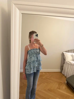 Blommig volang-linnetopp i blått - Supersöt blommig topp/kjol med volanger i blått och vitt. Den har flera lager volanger och ett smockat liv för extra komfort och stil. Kan användas som både kjol och topp. Finns ingen storlek på den men den passar som S men är stretchig så funkar nog för M och xs
