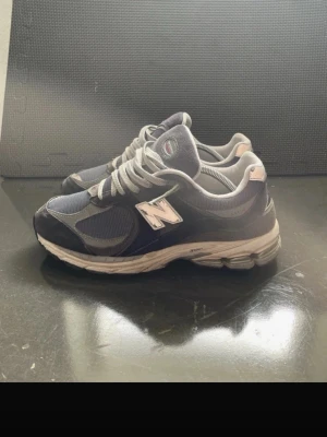 New Balance 2002r - Snygga New Balance 2002r sneakers i mörkgrått och silver med mesh och mockadetaljer. Klassisk N-logga på sidan och bekväm, vadderad sula. Perfekta för dig som gillar retrostil och streetwear.