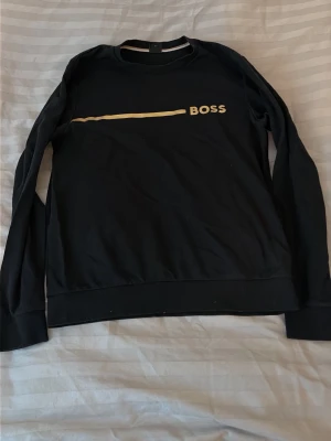 Svart långärmad topp från BOSS - Svart långärmad topp från BOSS med rund halsringning och ett stilrent tryck i vitt över bröstet. Tillverkad i mjukt material som känns skönt mot huden. Perfekt för dig som gillar enkel men snygg design.