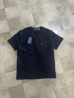 Svart Ralph Lauren T shirt - Köpte denna svarta Ralph Lauren t shirt men eftersom den var för liten behöver jag tyvärr sälja den. Den är helt ny och perfekt inför sommaren