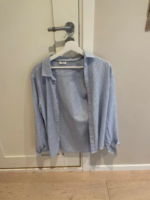 Blårandig skjorta i bomull - Klassisk blårandig skjorta med krage och långa ärmar. Skjortan har knappar framtill och är tillverkad i mjuk bomull. Perfekt för en avslappnad men ändå stilren look.