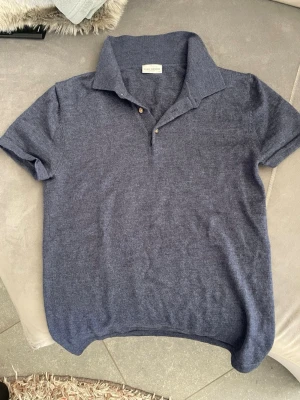 Blå piké tröja från John Henric - Klassisk blå polotopp från John Henric i merinoull. Tröjan har korta ärmar, krage och två knappar framtill. Enkel och stilren design som passar till mycket. Perfekt för dig som gillar en clean och tidlös look.