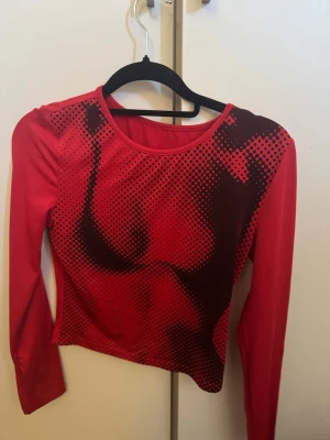 Röd långärmad topp med grafiskt tryck - Cool röd långärmad topp med svart grafiskt prickmönster framtill som ger en edgy look. Figurnära passform och rund halsringning. Perfekt för dig som vill sticka ut med en unik och trendig stil.