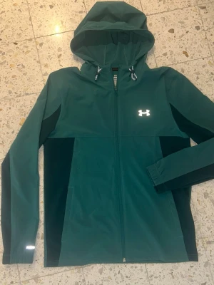 Under Armour vindjacka grön  - Mörkgrön hoodie från Under Armour med hel dragkedja och reflekterande logga på bröstet. Riktigt unik och fet har aldrig sett någon annan ha på sig den. Pris kan diskuteras vid snabb affär 