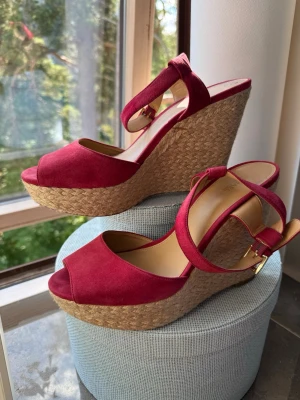 ljus hallonrosa  kilklackssandaler Michael Kors - Snygga r sandaler från Michael Kors med hög kilklack i flätad jute och öppen tå. Remmar i mockaimitation med justerbart spänne i guld. Perfekta för att lyfta vilken outfit som helst med sin trendiga och somriga look.