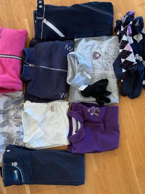 Ridkläder strl 130-140 - Ridkläder stl 130-140  Det är två ridbyxor 2 pikétröjor, en vit och en lila 1 långärmad T-shirt med ”bling” 1 varm fleece 2 zip-tröjor, en ljusgrå och en mörkgrå Dessutom fyra par strumpor och ett par fingervantar med ”gummiprickar”
