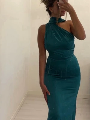 Mörkgrön oneshoulder långklänning - Snygg mörkgrön långklänning med oneshoulder-design och hög krage. Klänningen har en figurnära passform och är perfekt för dig som vill sticka ut med en elegant look. Aldrig kommit till användning! 