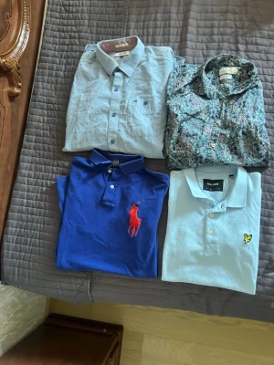 Blå pikétröja från Polo Ralph Lauren - Säljer en blå pikétröja från Polo Ralph Lauren med klassisk krage och två knappar. Tröjan har en stor röd broderad logga på bröstet och är tillverkad i mjuk bomull. Perfekt för en avslappnad men ändå stilren look.