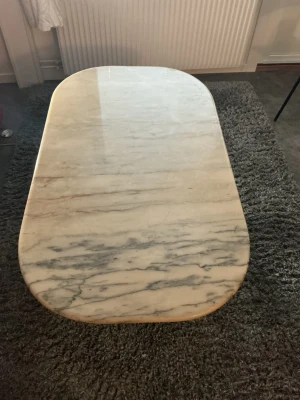 Ovalt soffbord i marmor och krom - Stilrent soffbord med oval bordsskiva i ljus marmor med grå ådring. Underredet är i kromat metall med böjda ben som ger en modern känsla. Perfekt som mittpunkt i vardagsrummet för dig som gillar tidlös design.