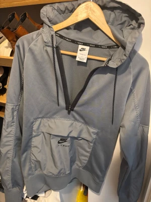 Nike Air Max grå hoodie med dragkedja - Snygg grå hoodie från Nike Air Max med halv dragkedja framtill och stor magficka med logga. Tillverkad i Therma-Fit material som håller värmen. Passar perfekt till alla årstider och är i storlek S.
