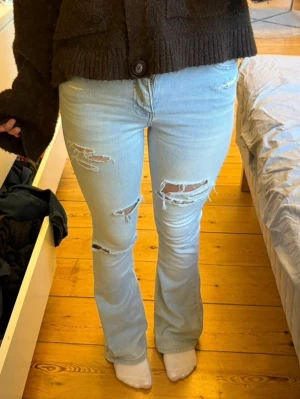 Ljusblå slitna bootcut jeans - Säljer ett par ljusblå bootcut jeans med flera slitningar och hål på låren och knäna🩵