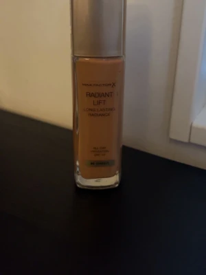Max Factor Radiant Lift Foundation Amber - Radiant Lift foundation från Max Factor i nyansen Amber. Kommer i en rektangulär glasflaska med guldfärgat lock. Ger långvarig lyster och har SPF 30. Perfekt för dig som vill ha en återfuktande bas med naturlig glow.