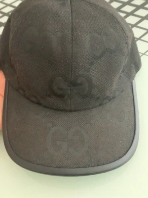 Svart jambo keps  - Snygg svart jambo keps  med det klassiska GG-monogrammet ton-i-ton över hela kepsen. Tillverkad i ett slitstarkt tyg med böjd skärm och justerbar baksida. Perfekt för dig som vill ha en stilren accessoar med lyxig känsla. Pris kan diskuteras vid snabb affär och byten ingår!!
