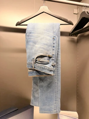 Tiger of Sweden  - Säljer ett par ljusblå jeans med klassisk femficksdesign och raka ben. Jeansen har en snygg läderpatch bak i midjan och subtila slitningar för en avslappnad look. Perfekta till sneakers eller boots och passar till många olika stilar.