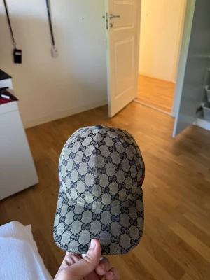Gucci beige keps med GG-mönster - Säljer en beige keps från Gucci med det klassiska GG-monogrammönstret över hela kepsen. Kepsen har böjd skärm och är tillverkad i ett slitstarkt tygmaterial. Perfekt för dig som vill ha en stilren och lyxig accessoar till din outfit.