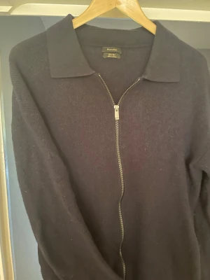 Mörkblå ulltröja med dragkedja - Snygg mörkblå tröja från Massimo Dutti i 100% ren ull. Tröjan har en klassisk krage och hel dragkedja framtill och fickor på sidan, vilket ger en stilren och modern look. Storlek L. Väldigt bra skick. 