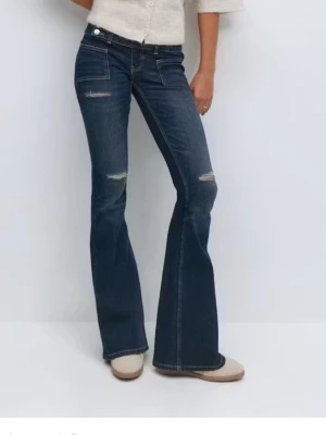 Mörkblå bootcut jeans med slitningar - Snygga mörkblå bootcut jeans med lätt slitna detaljer vid fickor och knän. Jeansen har klassisk femficksdesign, låg midja och utsvängda ben. Perfekta för dig som gillar en retroinspirerad look och vill ha ett par jeans som sticker ut.