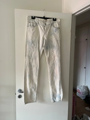 Vita slitna jeans med raka ben - Säljer ett par vita jeans med raka ben och distressed detaljer längs framsidan. Jeansen har klassisk femficksmodell och är tillverkade i denim. Perfekta för dig som gillar en avslappnad och trendig stil.
