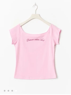Rosa topp med texttryck från gina  - Söt rosa topp med texten 'Dansar vidare i livet' broderat framtill. Modellen är tight och har korta ärmar med en något fyrkantig ringning. Perfekt för dig som gillar en enkel men personlig stil.