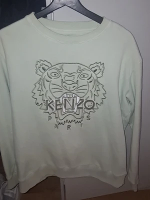Ljusgrön Kenzo sweatshirt med tiger - Cool ljusgrön sweatshirt från Kenzo med det ikoniska tigermotivet broderat framtill och texten 'Kenzo Paris' under. Tröjan har rund halsringning och ribbade muddar vid ärmslut och nederkant. Perfekt för dig som gillar streetwear och vill sticka ut. St smal myclet fin skick tar väl hand om mina saker 